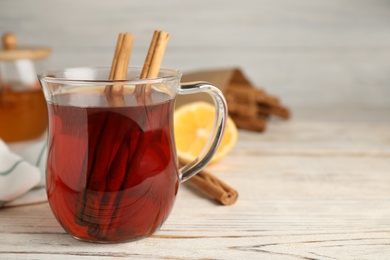 Glass cup of hot tea with aromatic cinnamon on white wooden table, closeup. Space for text