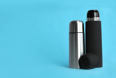 Stylish thermo bottles on light blue background, space for text
