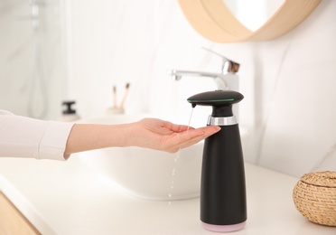 Photo of Woman using automatic soap dispenser in bathroom, closeup