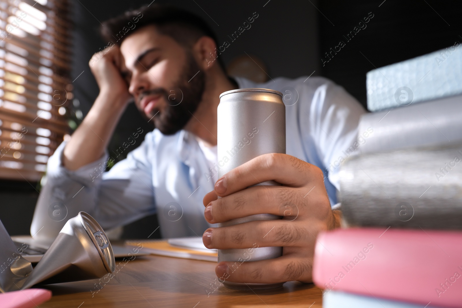 Photo of Tired young man with energy drink studying at home, focus on hand