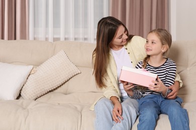 Photo of Young woman and her daughter with gift on sofa at home