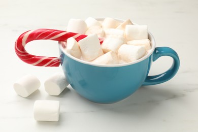 Photo of Tasty hot chocolate with marshmallows and candy cane on white marble table, closeup