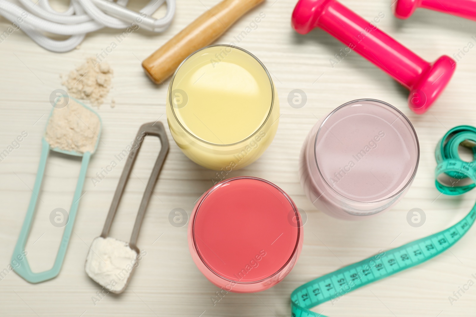 Photo of Tasty shakes, sports equipment, measuring tape and different powders on wooden table, flat lay. Weight loss