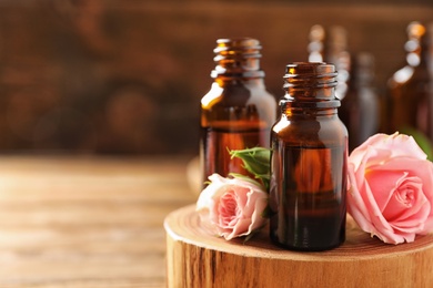 Photo of Bottles of rose essential oil and fresh flowers on table, closeup. Space for text