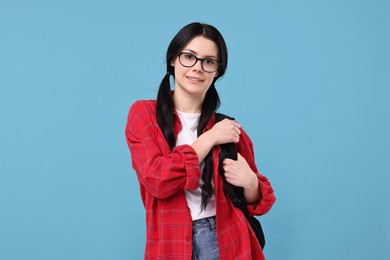 Smiling student in glasses with backpack on light blue background