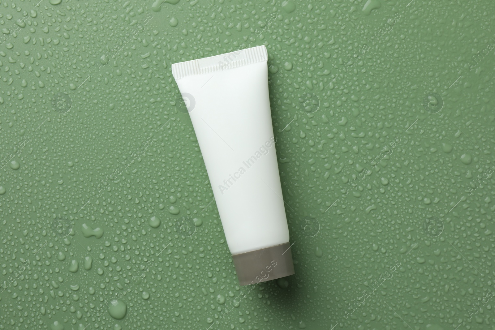 Photo of Moisturizing cream in tube on green background with water drops, top view