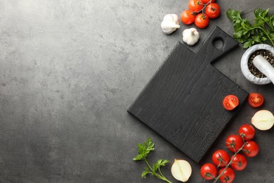Flat lay composition with black wooden cutting board and products on dark textured table. Space for text