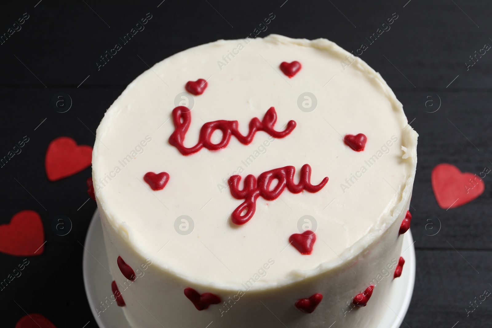 Photo of Bento cake with text Love You and paper hearts on black table, closeup. St. Valentine's day surprise