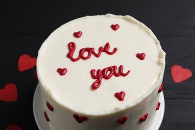 Photo of Bento cake with text Love You and paper hearts on black table, closeup. St. Valentine's day surprise