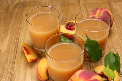 Photo of Glasses of peach juice, fresh fruits and leaves on wooden table