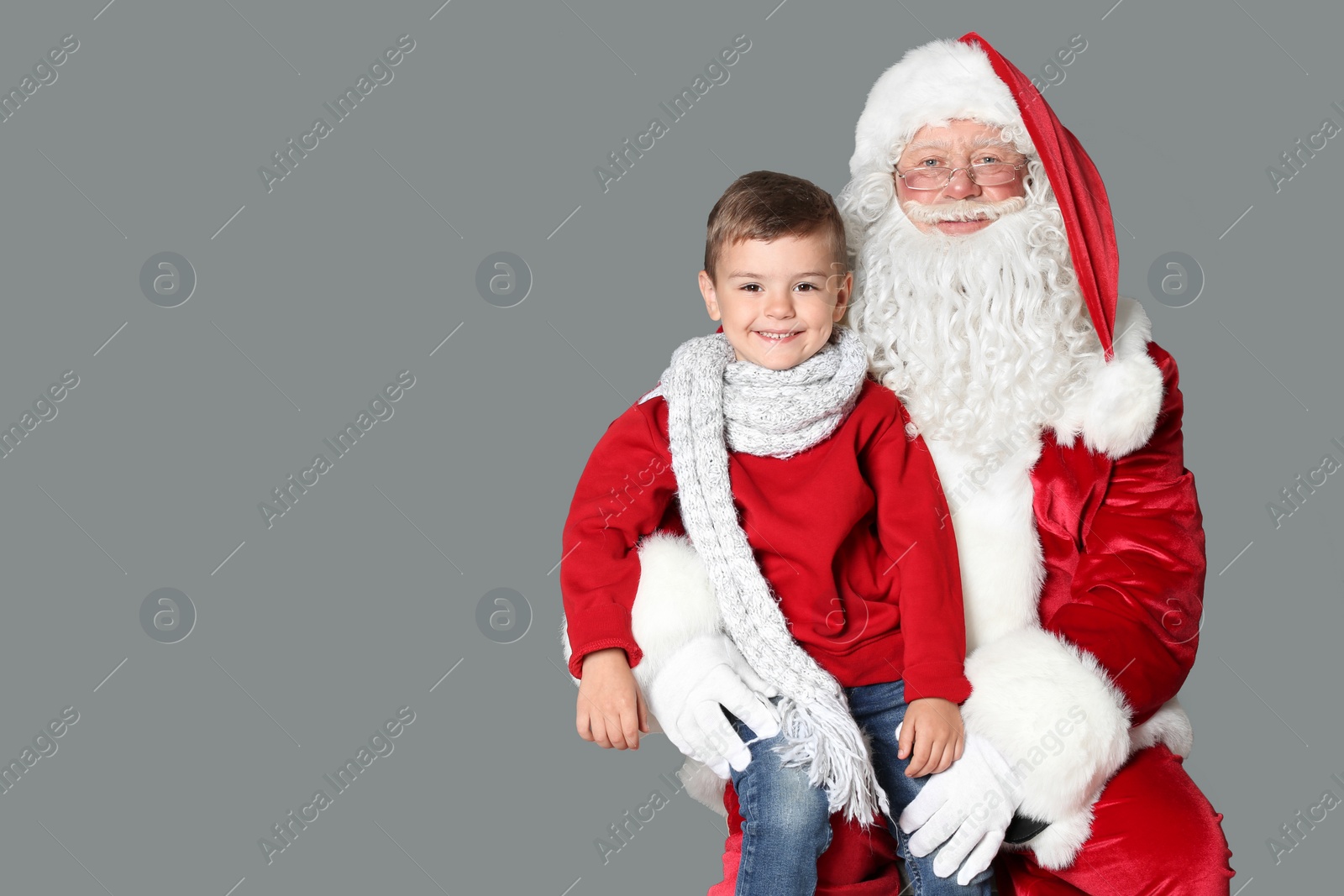 Photo of Little boy sitting on authentic Santa Claus' lap against grey background