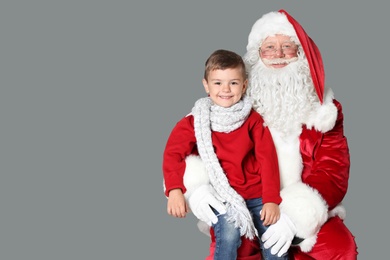 Photo of Little boy sitting on authentic Santa Claus' lap against grey background
