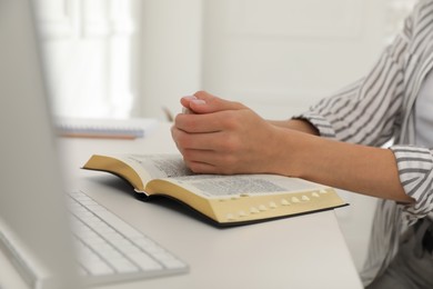 Photo of Young woman praying over Bible at desk, closeup