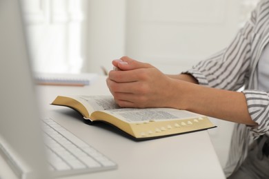 Young woman praying over Bible at desk, closeup