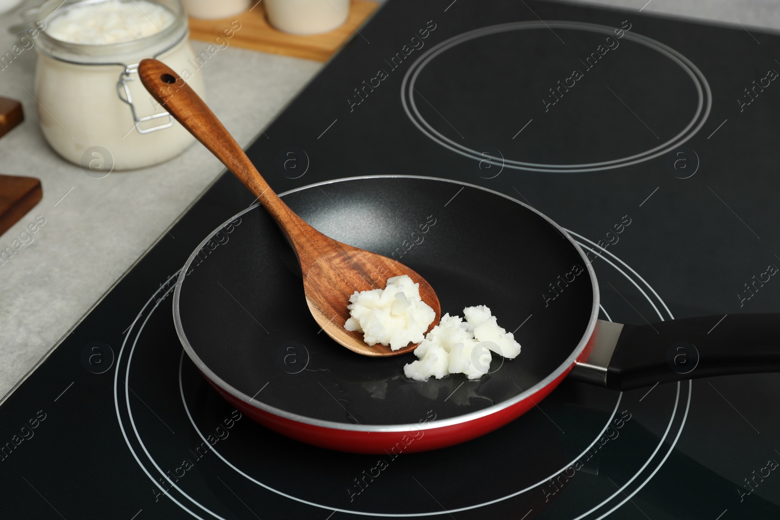 Photo of Frying pan with coconut oil and wooden spatula on induction stove. Healthy cooking