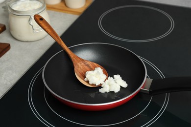 Frying pan with coconut oil and wooden spatula on induction stove. Healthy cooking