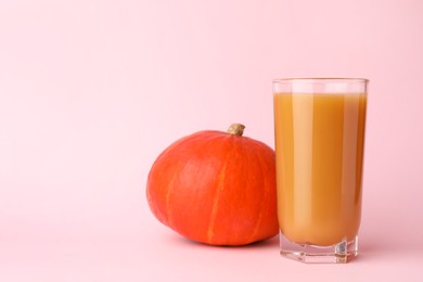 Tasty pumpkin juice in glass and whole pumpkin on pink background