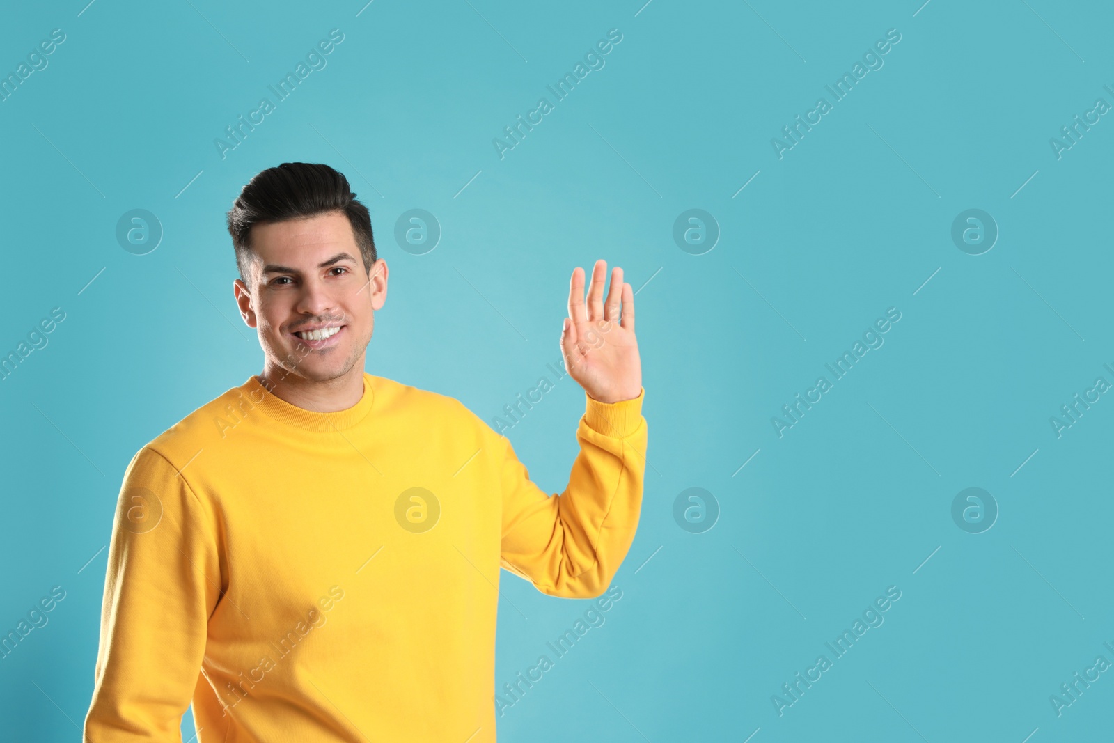 Photo of Cheerful man waving to say hello on turquoise  background, space for text