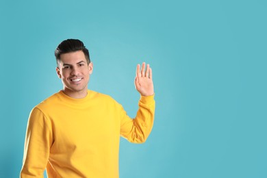 Photo of Cheerful man waving to say hello on turquoise  background, space for text