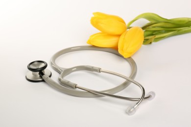 Photo of Stethoscope and yellow tulips on white background. Happy Doctor's Day