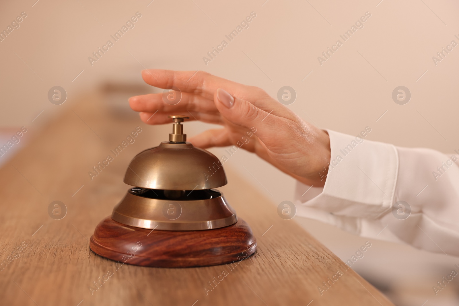 Photo of Woman ringing hotel service bell at wooden reception desk, closeup