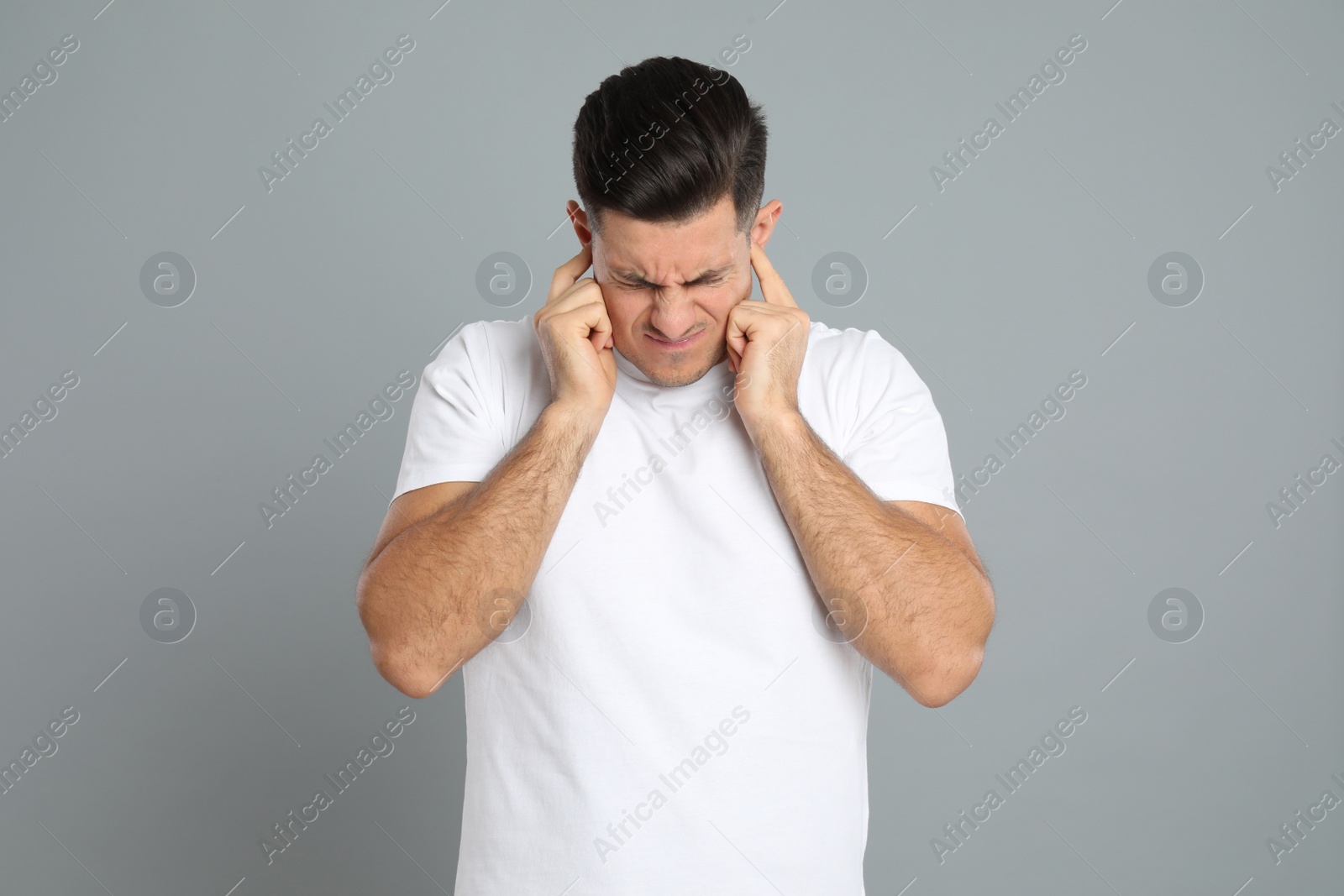 Photo of Emotional man covering ears with fingers on grey background