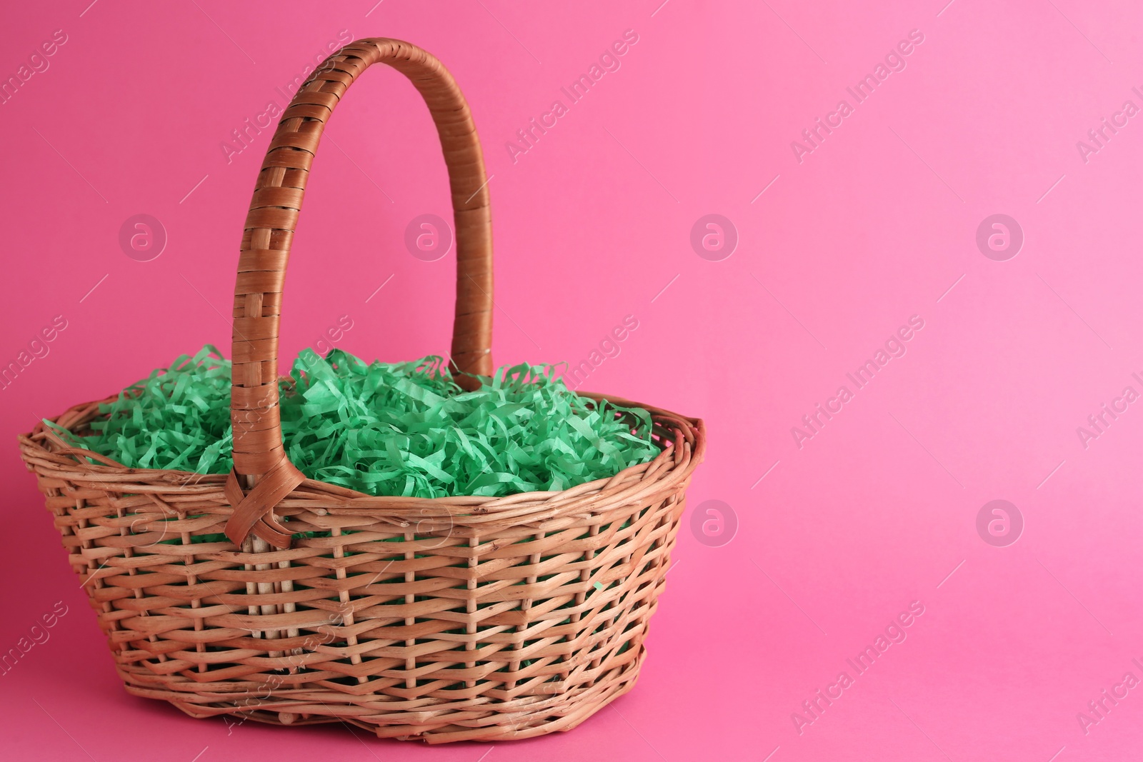 Photo of Easter basket with green paper filler on pink background, space for text