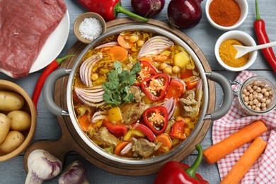 Saucepan of delicious vegetable soup with beef and ingredients on light gray table, flat lay