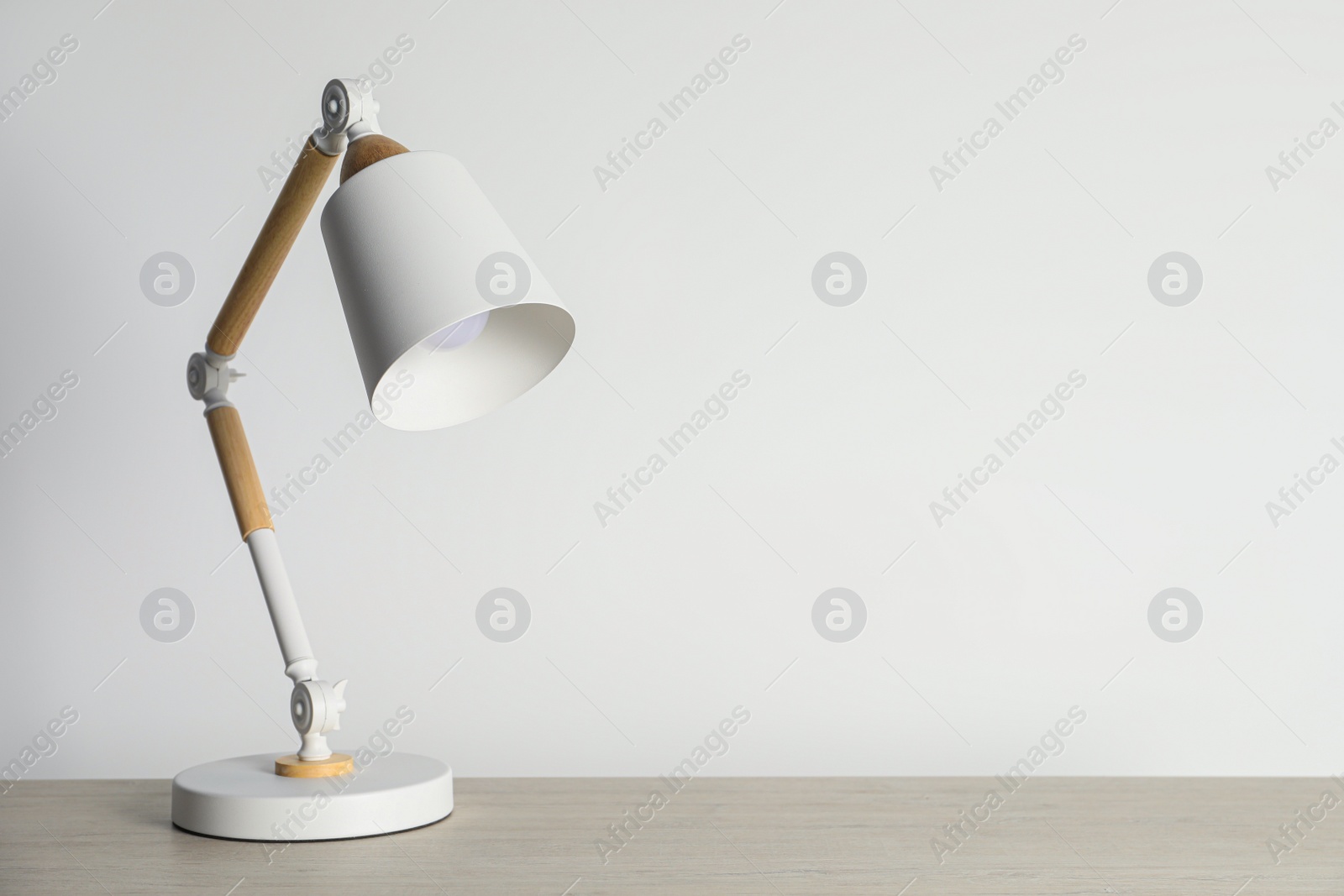 Stylish modern desk lamp on wooden table near white wall, space for text Photo of Stylish modern desk lamp on wooden table near white wall, space for text