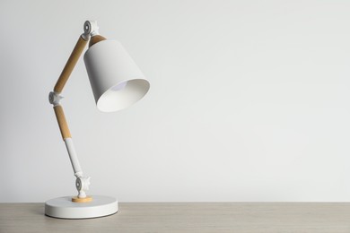 Photo of Stylish modern desk lamp on wooden table near white wall, space for text