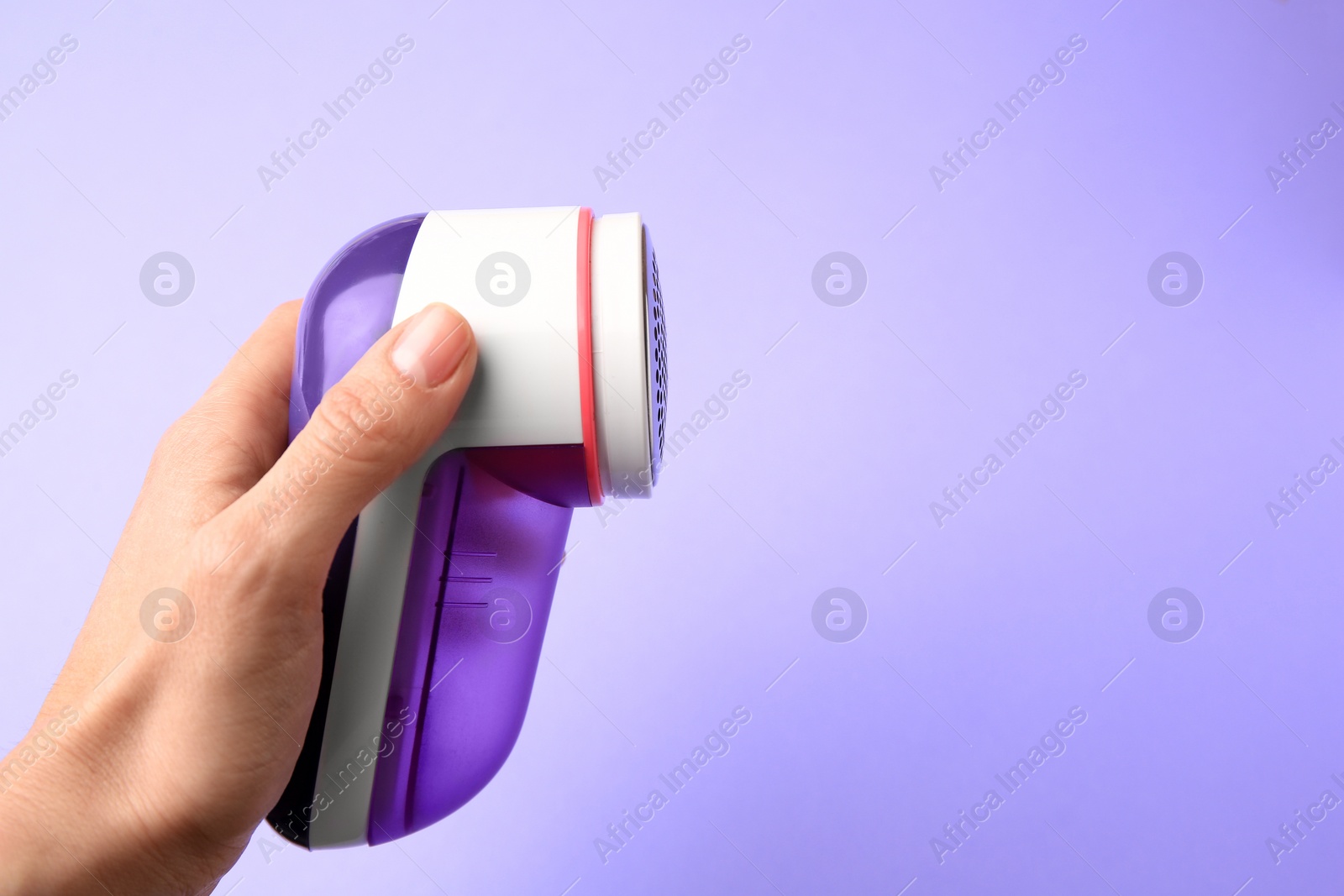 Photo of Woman holding modern fabric shaver on violet background, closeup. Space for text