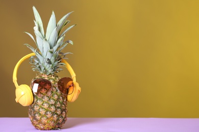 Photo of Pineapple with headphones and sunglasses on table against color background. Space for text