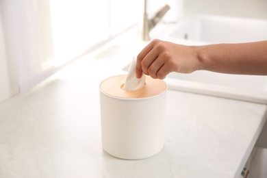 Photo of Woman taking paper tissue out of box on white countertop in kitchen, closeup