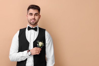 Handsome young groom with boutonniere on beige background, space for text. Wedding accessory