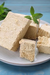 Photo of Pieces of tasty halva and mint on light blue wooden table, closeup