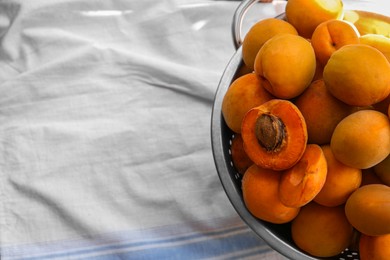 Photo of Colander with delicious ripe apricots on tablecloth, top view. Space for text