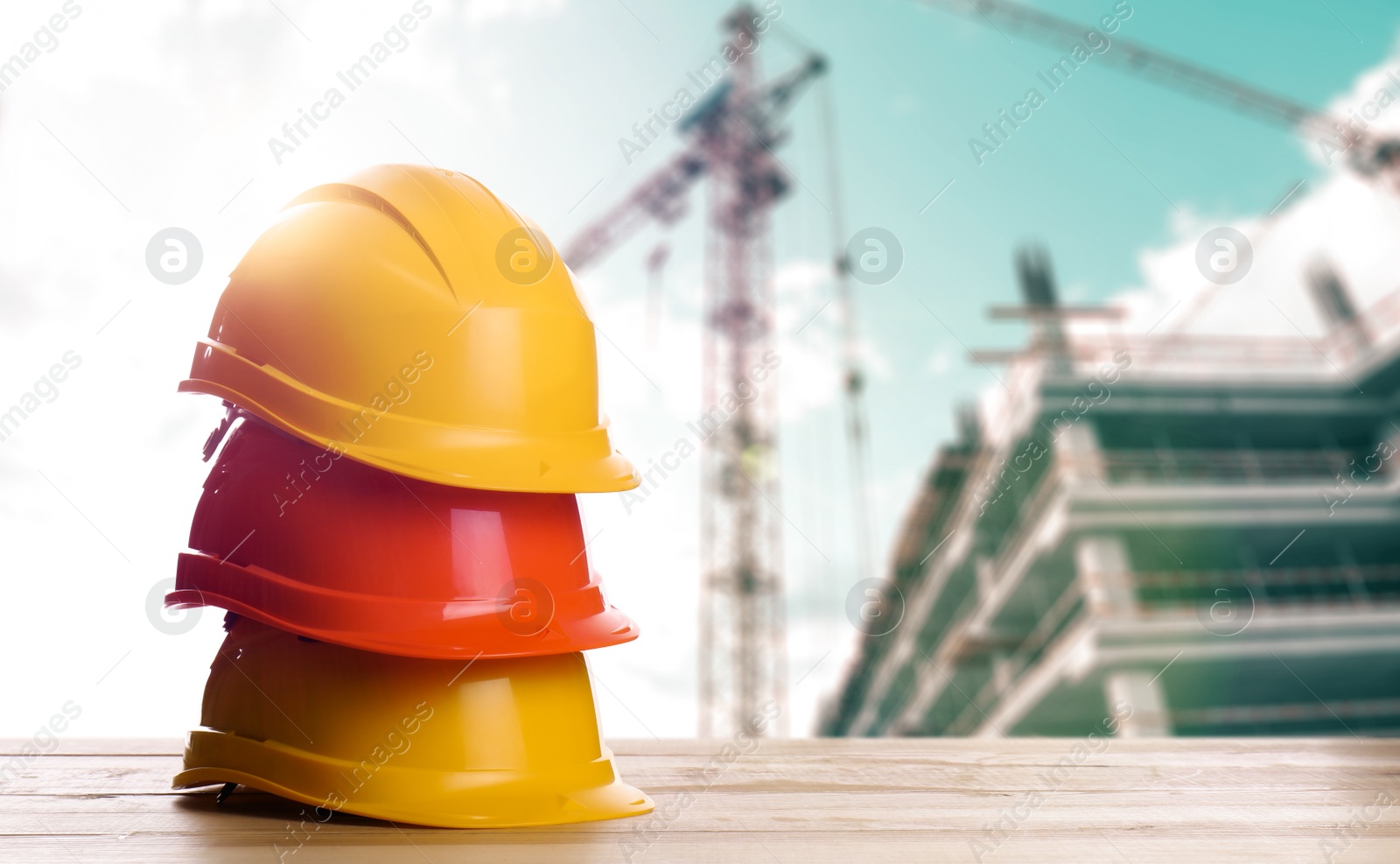 Image of Hard hats on wooden surface at construction site with unfinished building. Space for text 