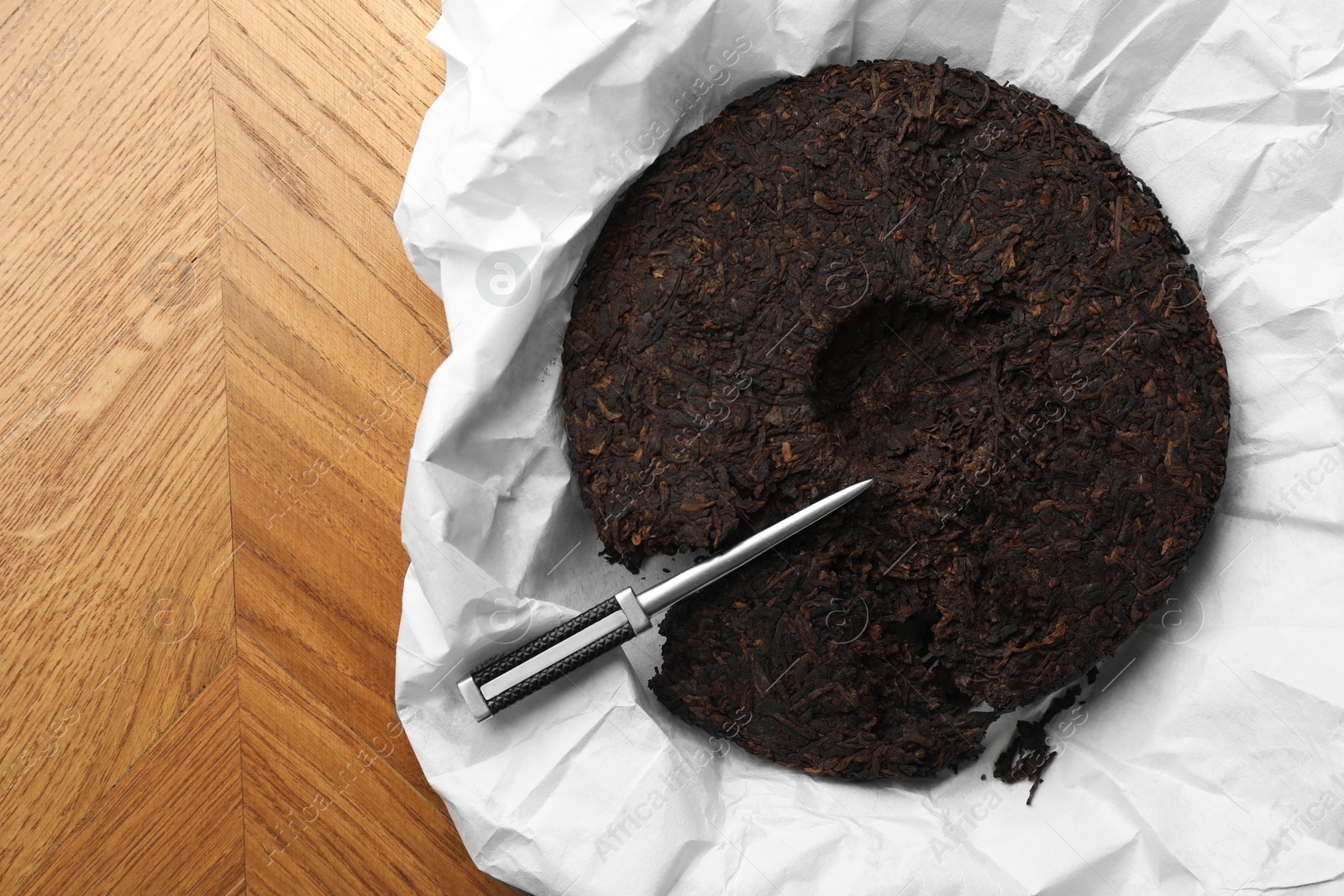 Photo of Disc shaped pu-erh tea and knife on wooden table, top view. Space for text