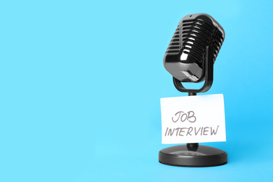 Photo of Retro microphone and reminder note with words JOB INTERVIEW on light blue background, space for text
