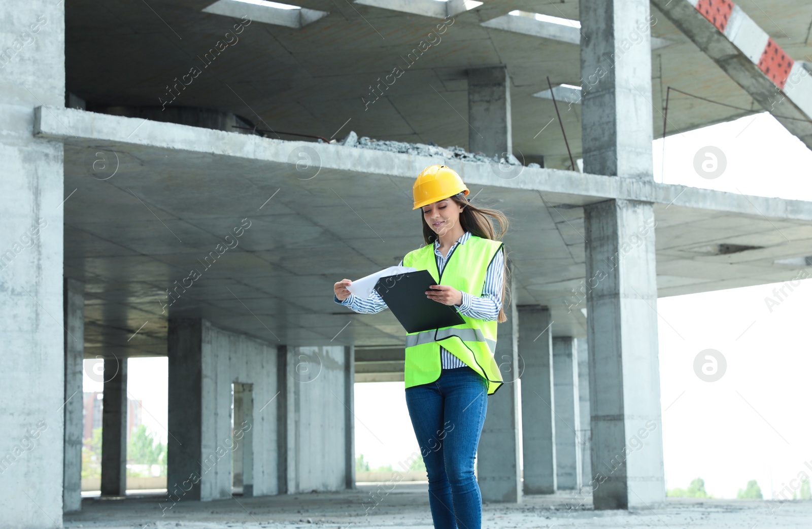 Photo of Professional engineer in safety equipment with clipboard at construction site