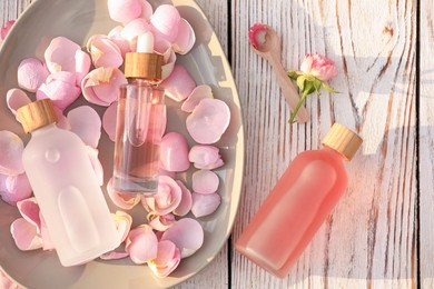 Bottles of rose essential oil and flowers on white wooden table, flat lay