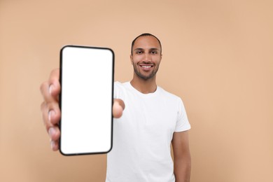 Young man showing smartphone in hand on beige background