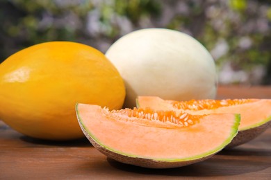 Whole and cut ripe melons on wooden table outdoors