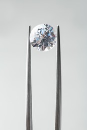 Photo of Tweezers with beautiful shiny diamond on light gray background, closeup