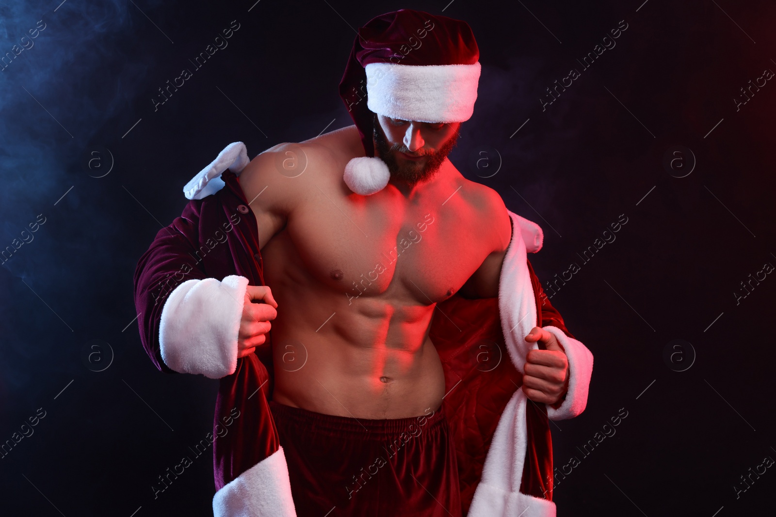 Photo of Attractive young man with muscular body in Santa costume on black background