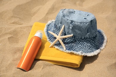 Sunscreen, panama hat, starfish and towel on sandy beach. Sun protection