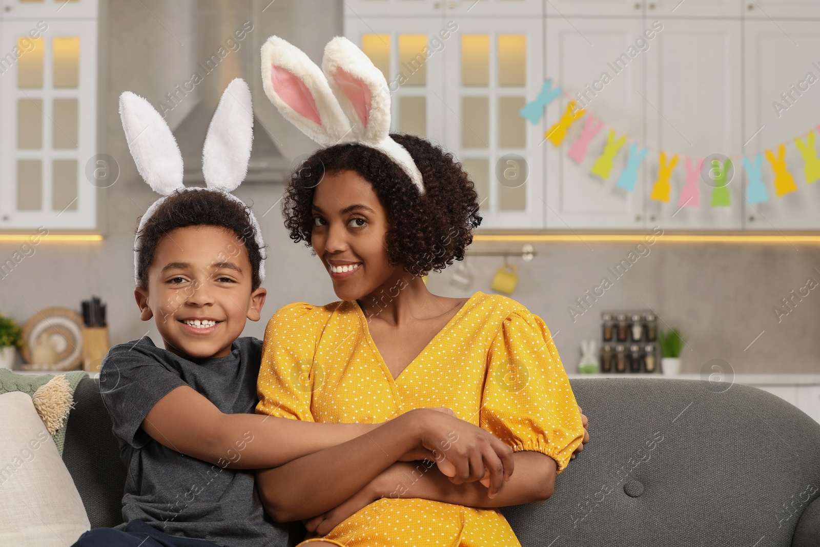 Photo of Happy African American mother and her cute son in bunny ears headband indoors. Easter celebration