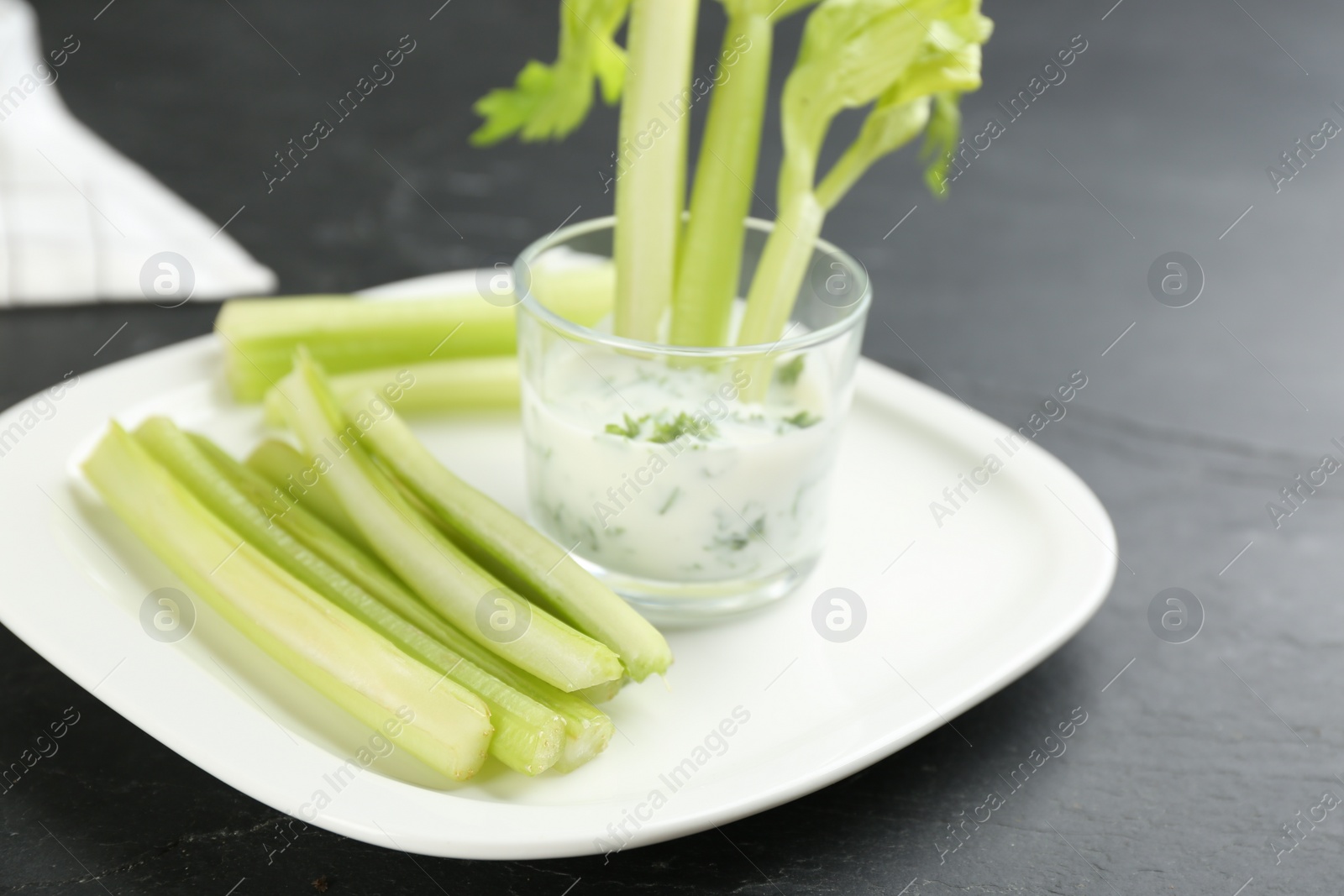 Photo of Celery sticks with dip sauce in glass on black table, closeup