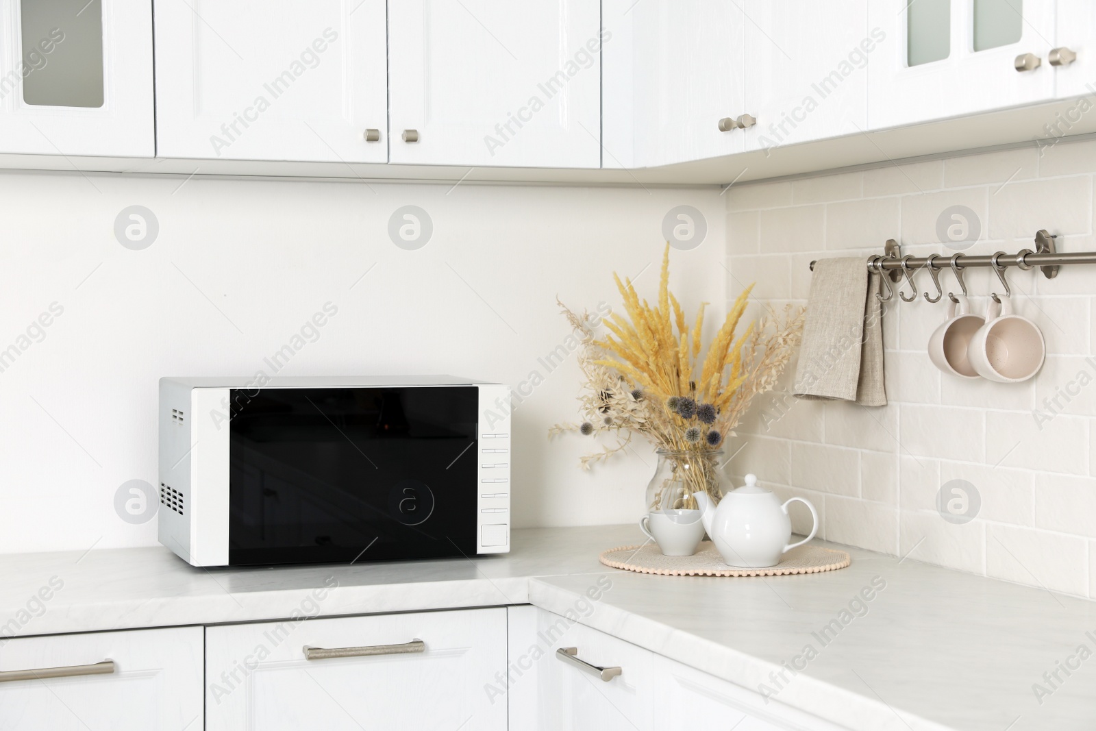 Photo of Modern microwave oven, dry flowers, cup and teapot on countertop in kitchen