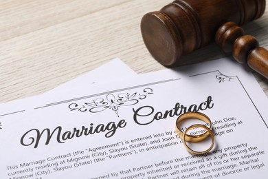 Photo of Marriage contract, golden wedding rings and gavel on wooden table, closeup